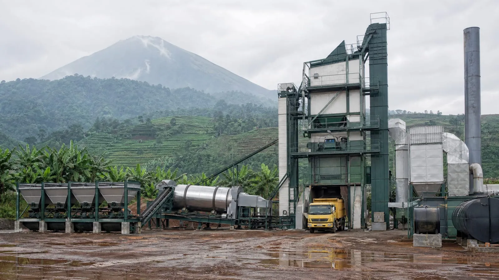 AMP batching di proyek jalan dengan perbukitan berteras dan gunung berapi di kejauhan (ilustrasi)