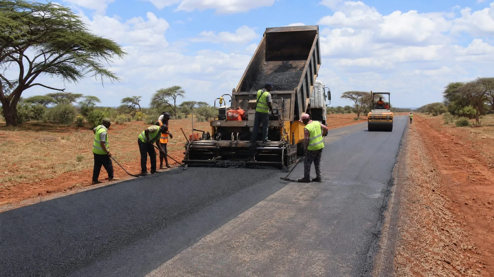 Road crew placing an asphalt overlay with a paver, roller and tipping truck